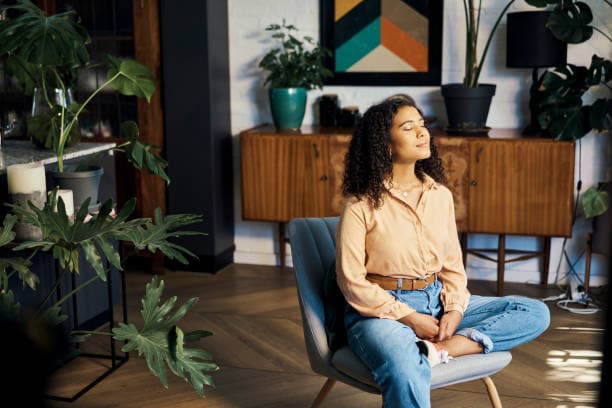 A person sitting peacefully in a softly lit room surrounded by natural textures and plants