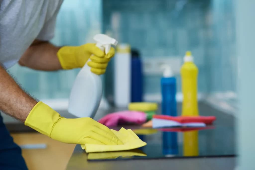 A collection of cleaning supplies including a spray bottle and a cloth being used to wipe down a surface