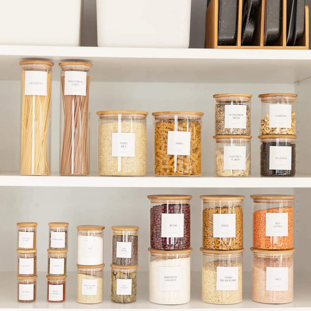 Neatly arranged clear glass kitchen jars with wooden lids on a shelf